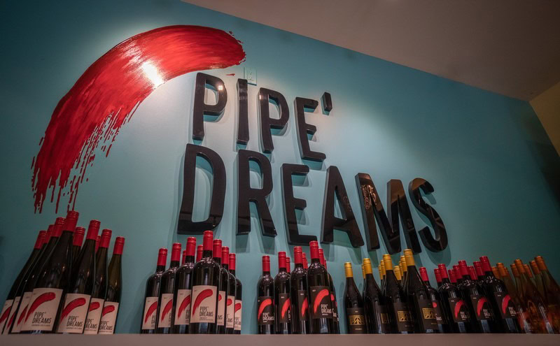 Wine bottles arranged under a sign that says 'Pipe Dreams' in a wine shop or tasting room.